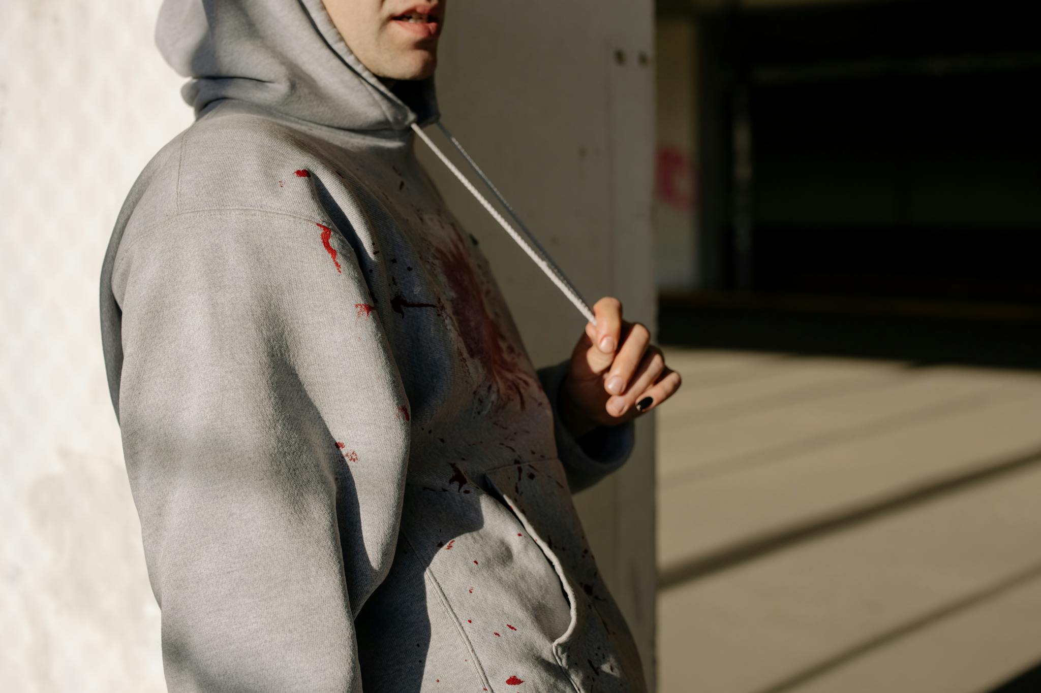 A close-up of a person in a gray hoodie with paint splatters in an urban setting.