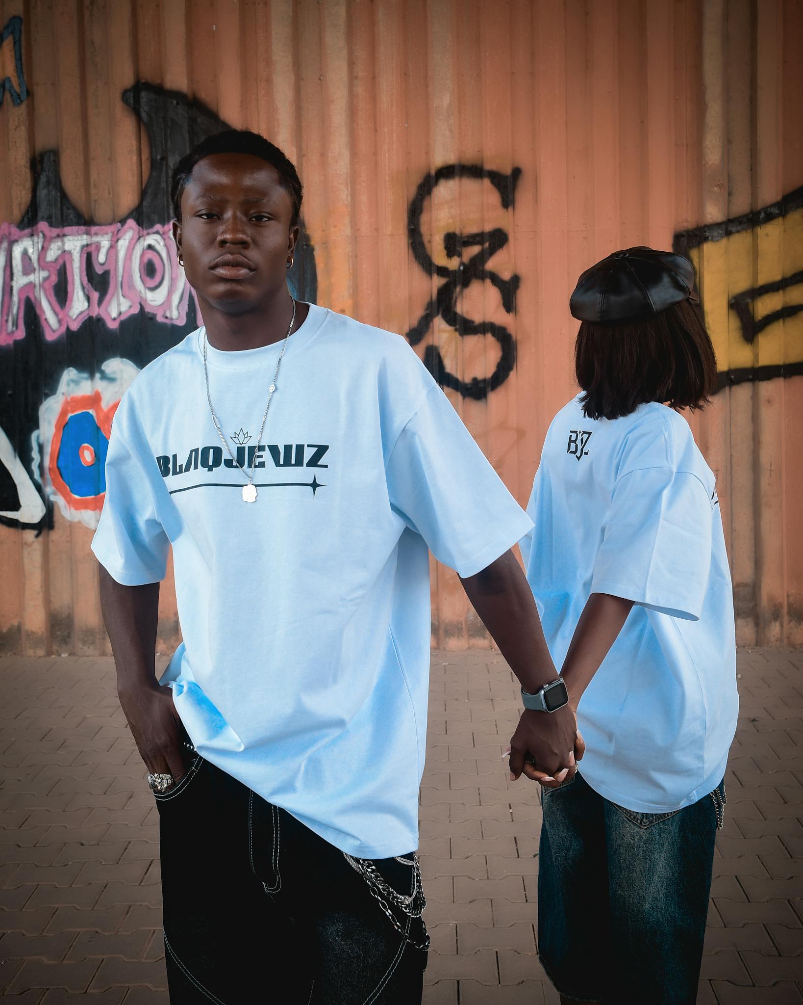 Two individuals wearing matching t-shirts pose before vibrant graffiti art outdoors.